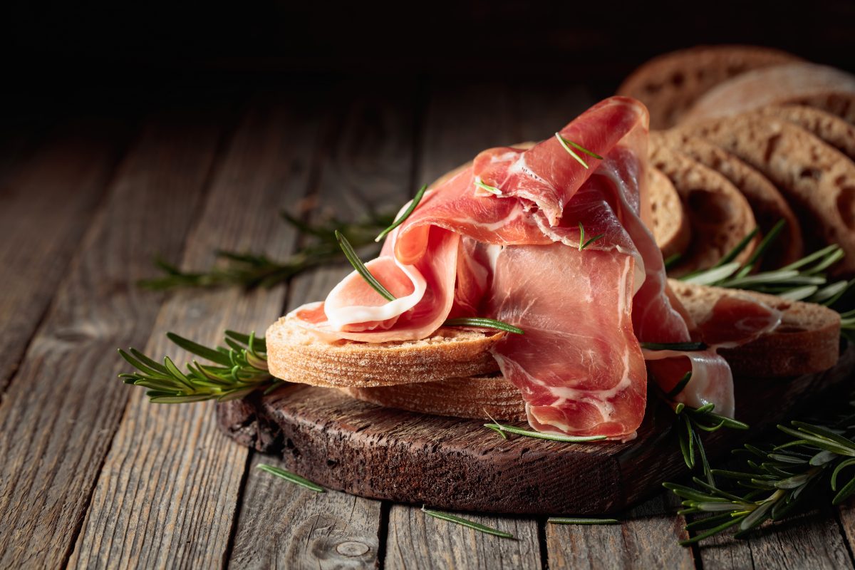 Prosciutto with bread and rosemary on an old wooden table. Copy space.